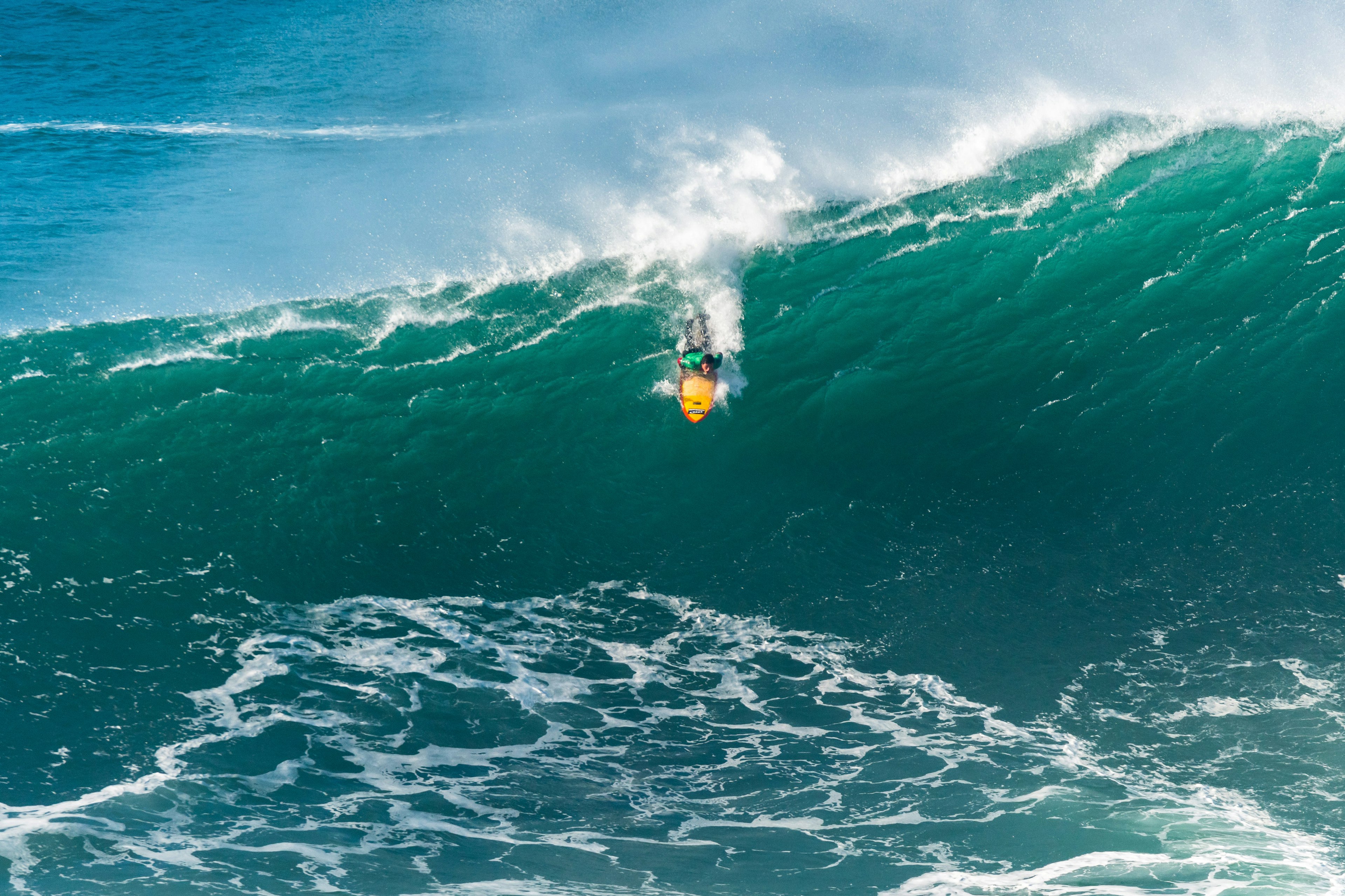 A surfer on a yellow board heads down a giant wave