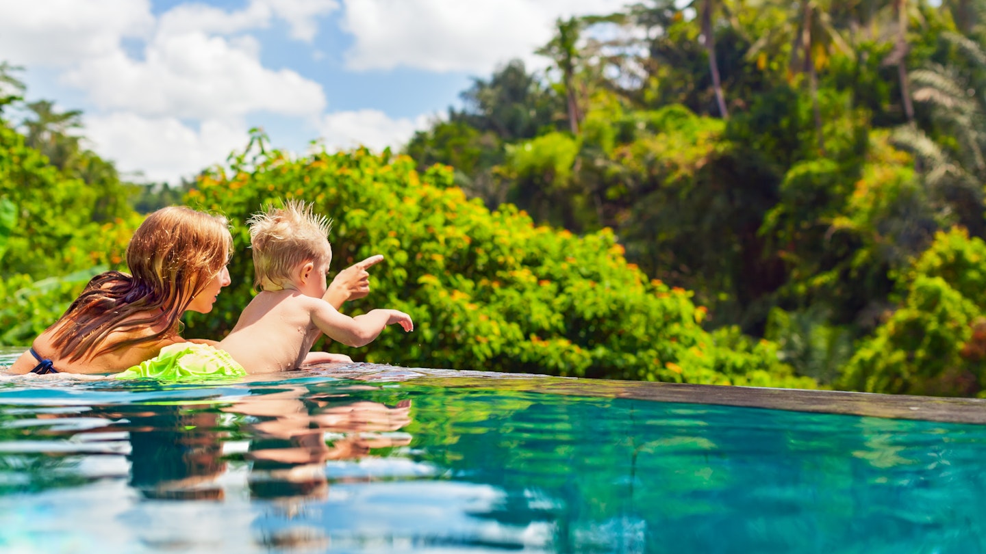 Family Bali beach holiday concept. Happy son with mother - active baby at poolside in infinity swimming pool. Summer healthy lifestyle and children water activity, games and lessons with parents.