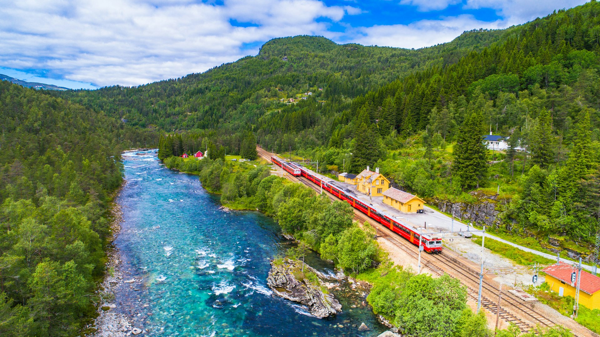The Oslo to Bergen train runs along a railway track beside a blue river in Norway.