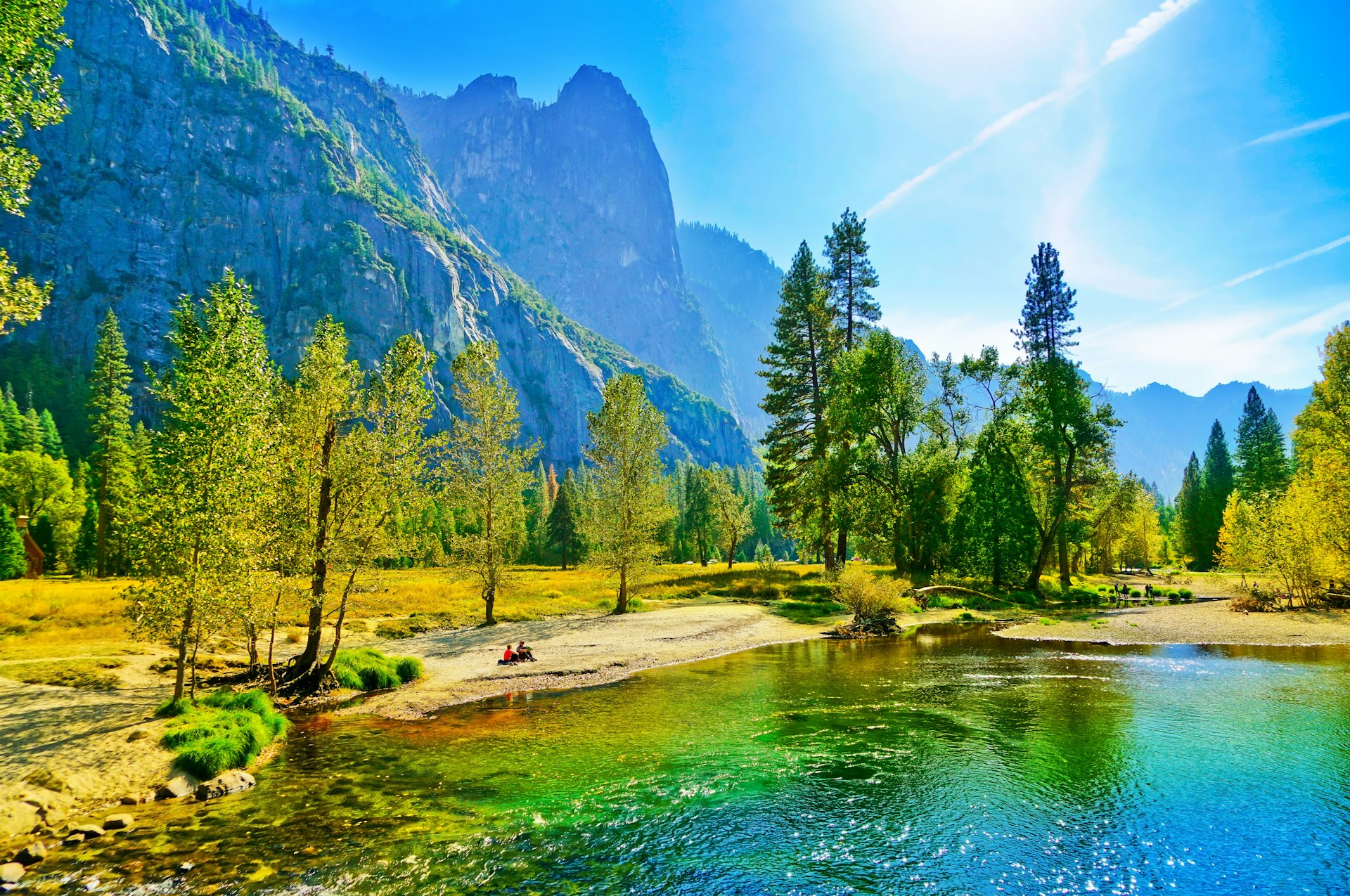 People sit on the banks of the Merced River in Yosemite Valley in the fall.