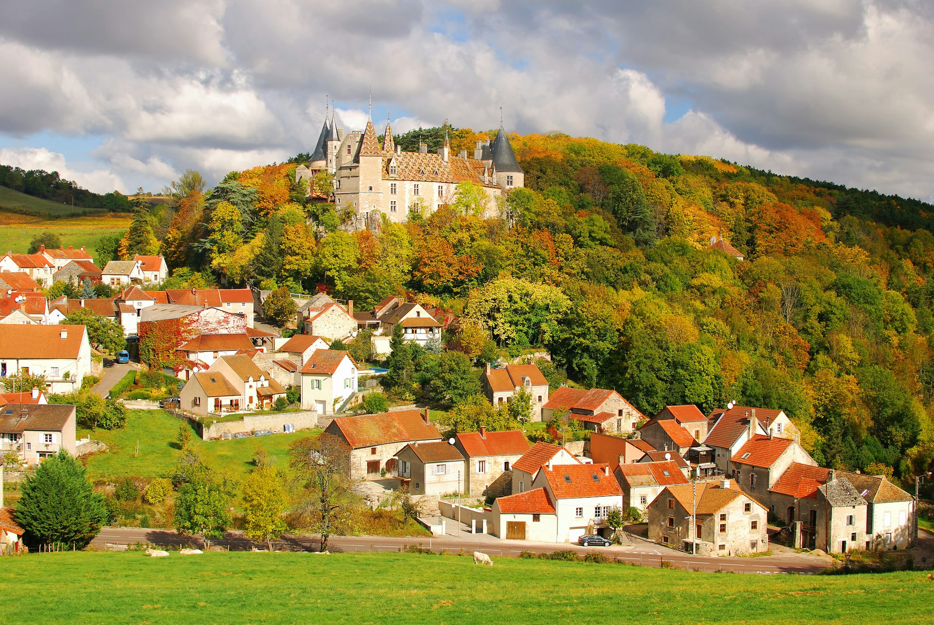 A huge fortress-style chateau rises above a village in a wooded area