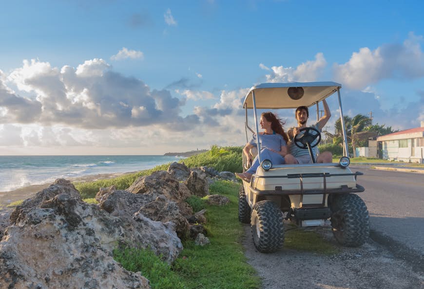 Ett par som kör en golfbil på en tropisk strand på Isla Mujeres, Mexiko