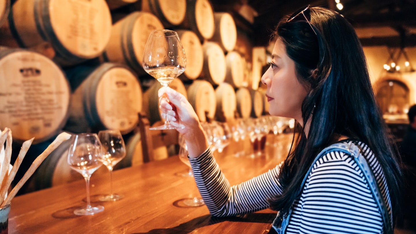 Young woman in the wine cellar tasting white wine alcohol. professional wine steward sitting indoor napa valley restaurant concentrated looking at glass. elegant lady relax in grapery bar