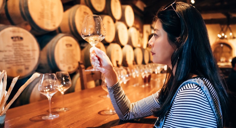 Young woman in the wine cellar tasting white wine alcohol. professional wine steward sitting indoor napa valley restaurant concentrated looking at glass. elegant lady relax in grapery bar