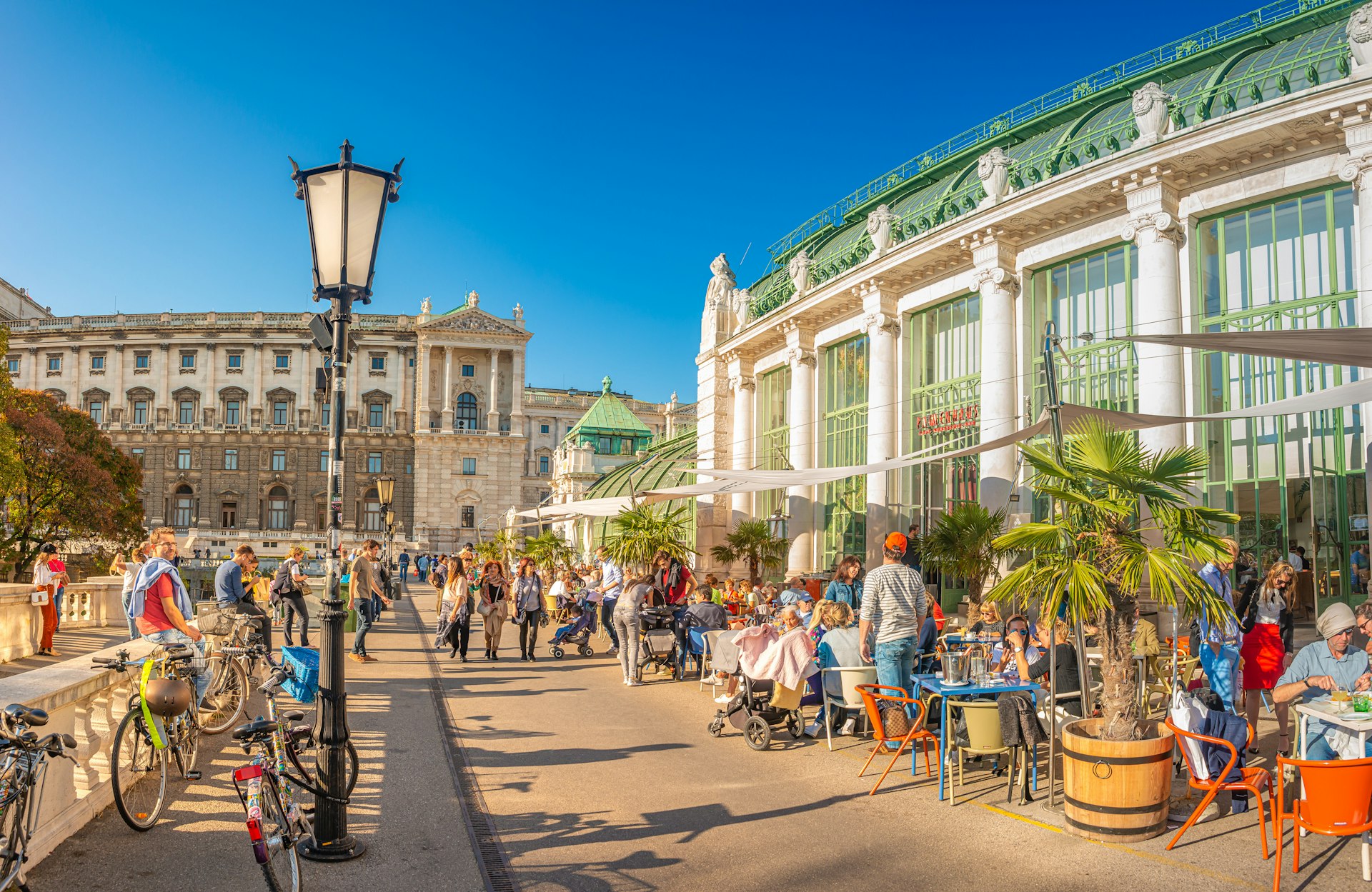 People sit at tables lining a busy walkway close to the Hofburg Palace in Vienna in the heart of summer.
