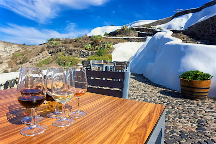 Plusieurs verres de vin se tiennent sur une table à l'extérieur d'un petit bâtiment en pierre blanche