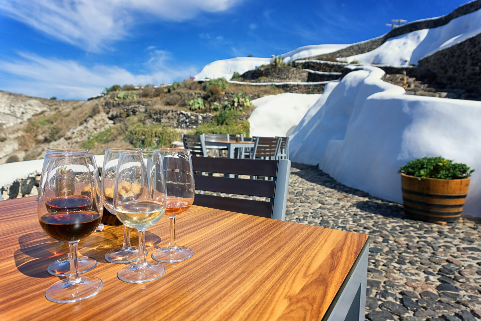 Several glasses of wine stand on a table outside a small white stone building