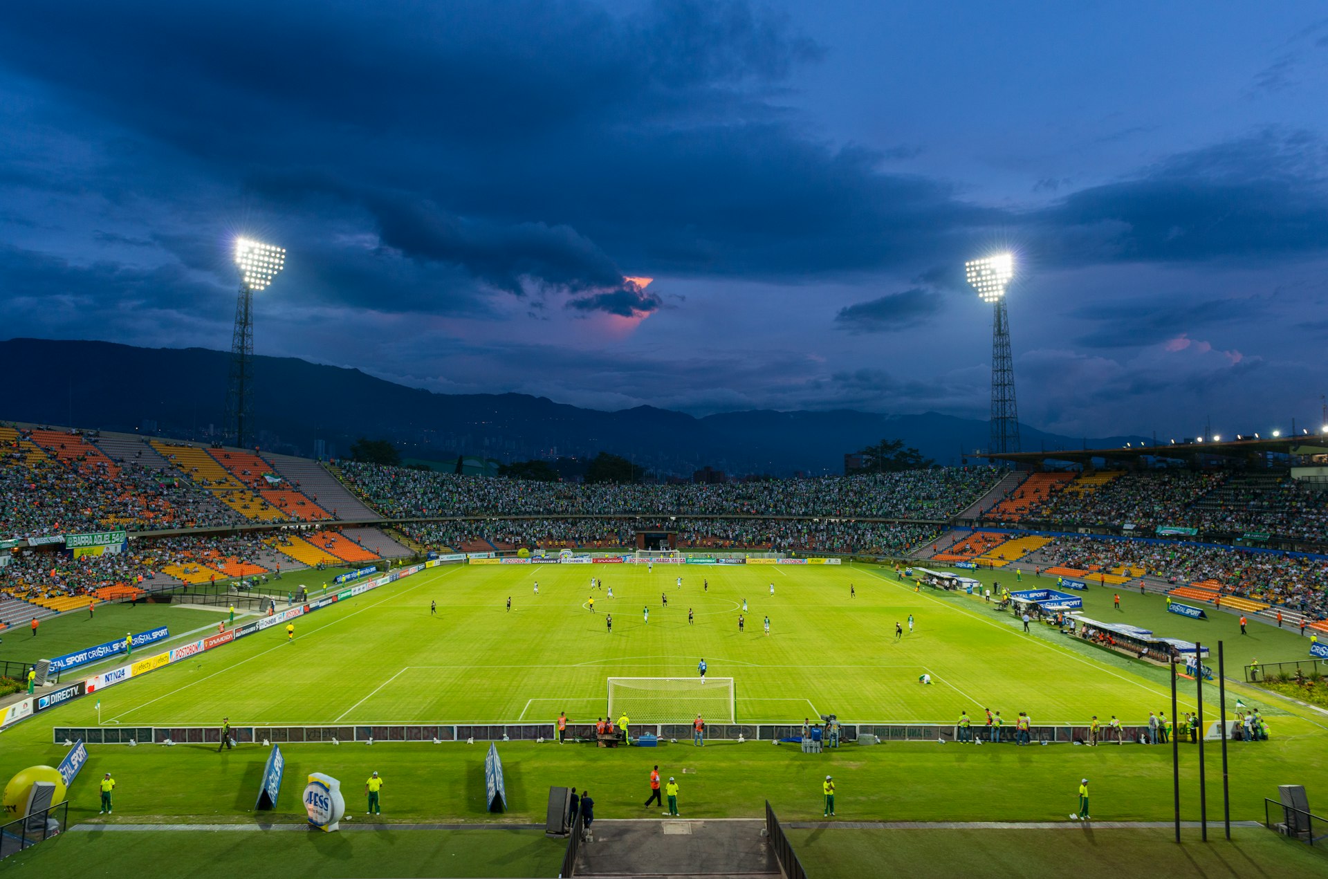 A shot taken within a stadium of players on a football field lit up by floodlights