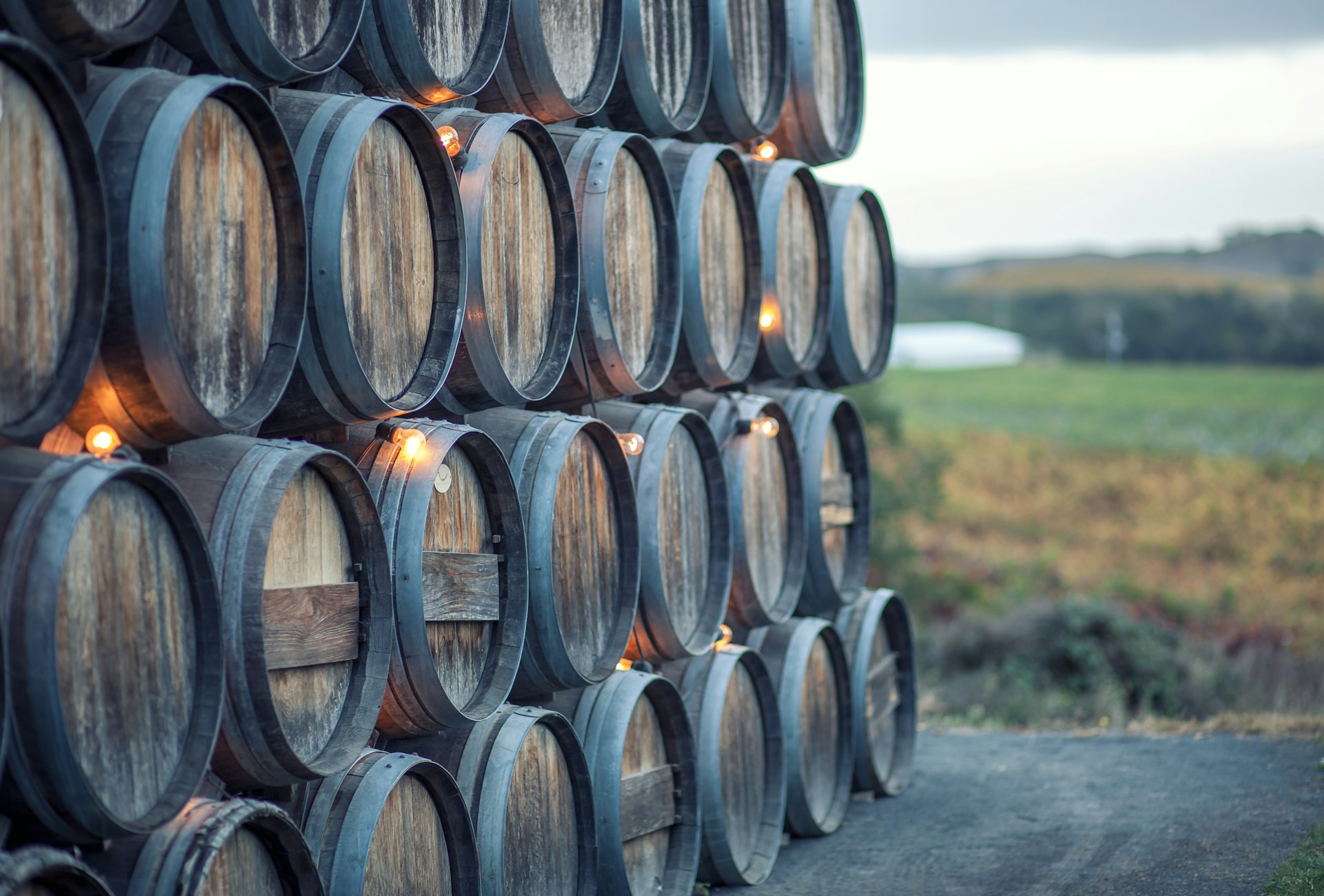 Stacked rustic oak barrels near a vineyard in California wine country