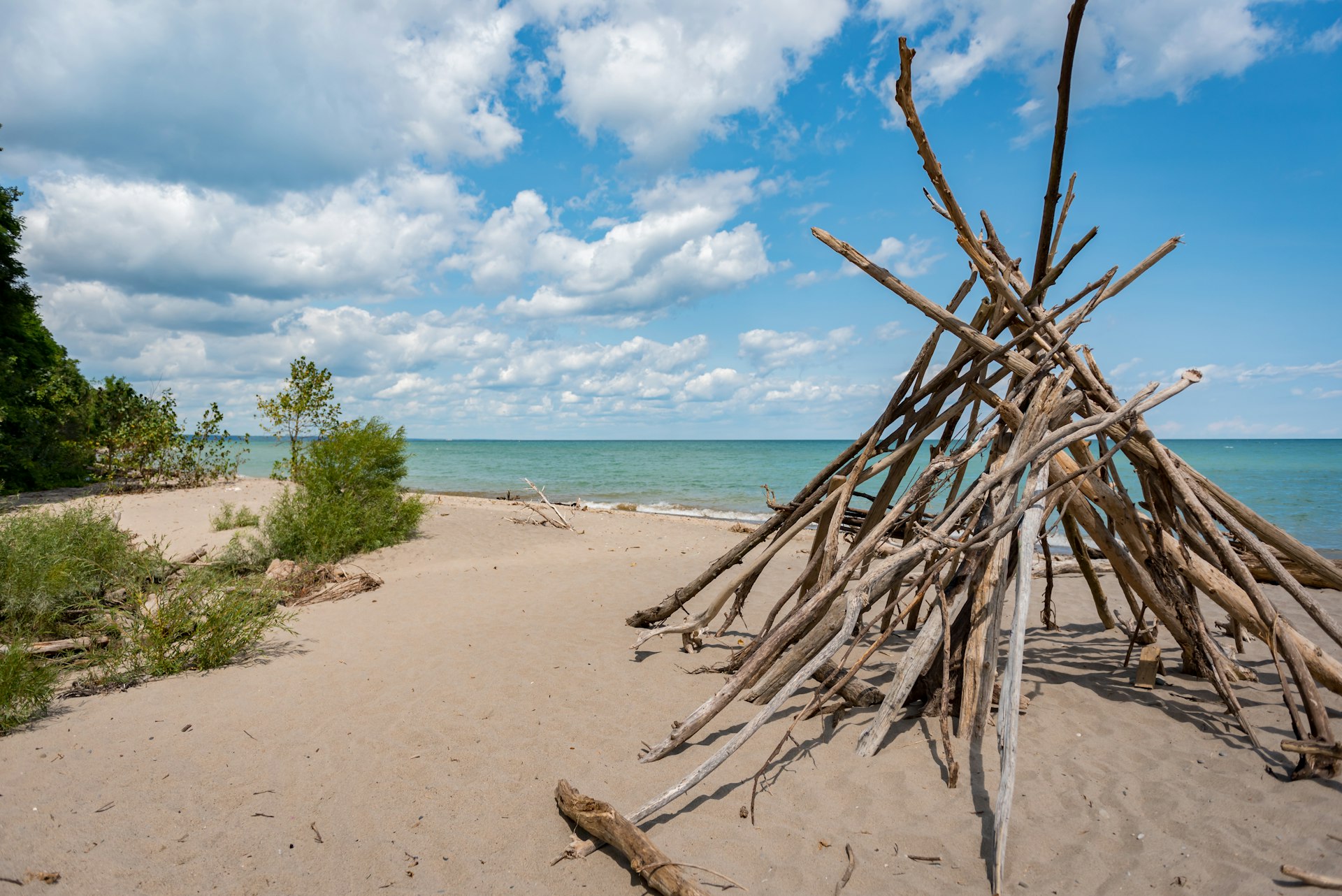 A series of large sticks piled together to form a teepee-like structure on an empty sandy beach