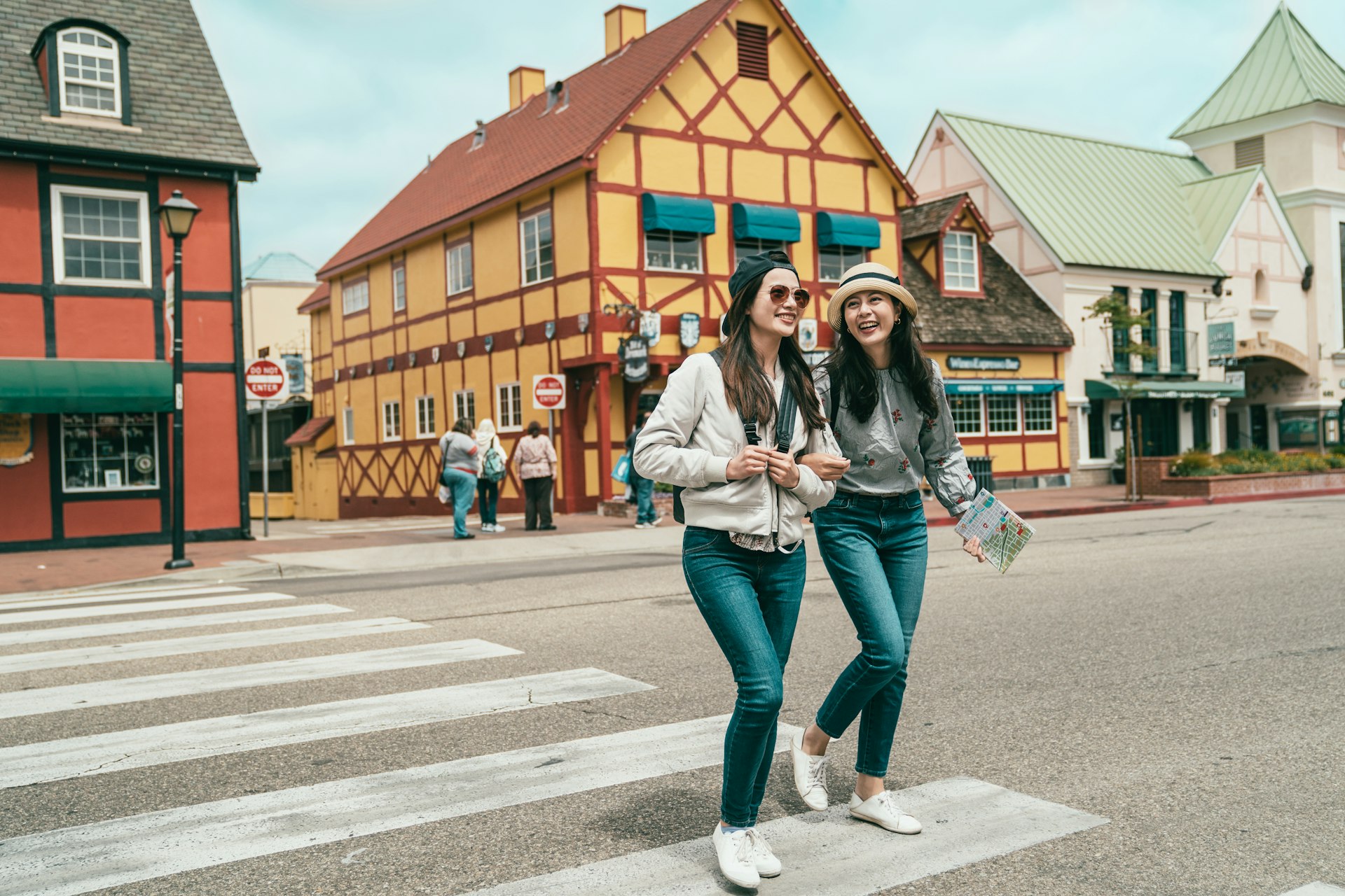 Two women walk across a road lined with buildings with Danish-style architecture