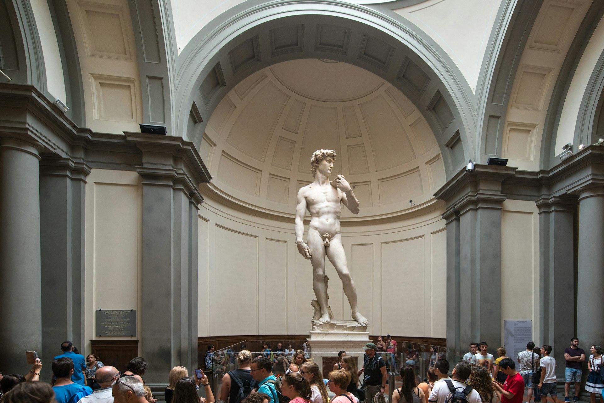 Crowds congregate in front Michelangelo’s David, displayed under stone arches and among columns at the Accademia di Belle Arti di Firenze