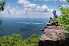 A chinese woman sitting on the edge of a cliff on top of overlook mountain in the catskills in Woodstock New York on a sunny summer day.;