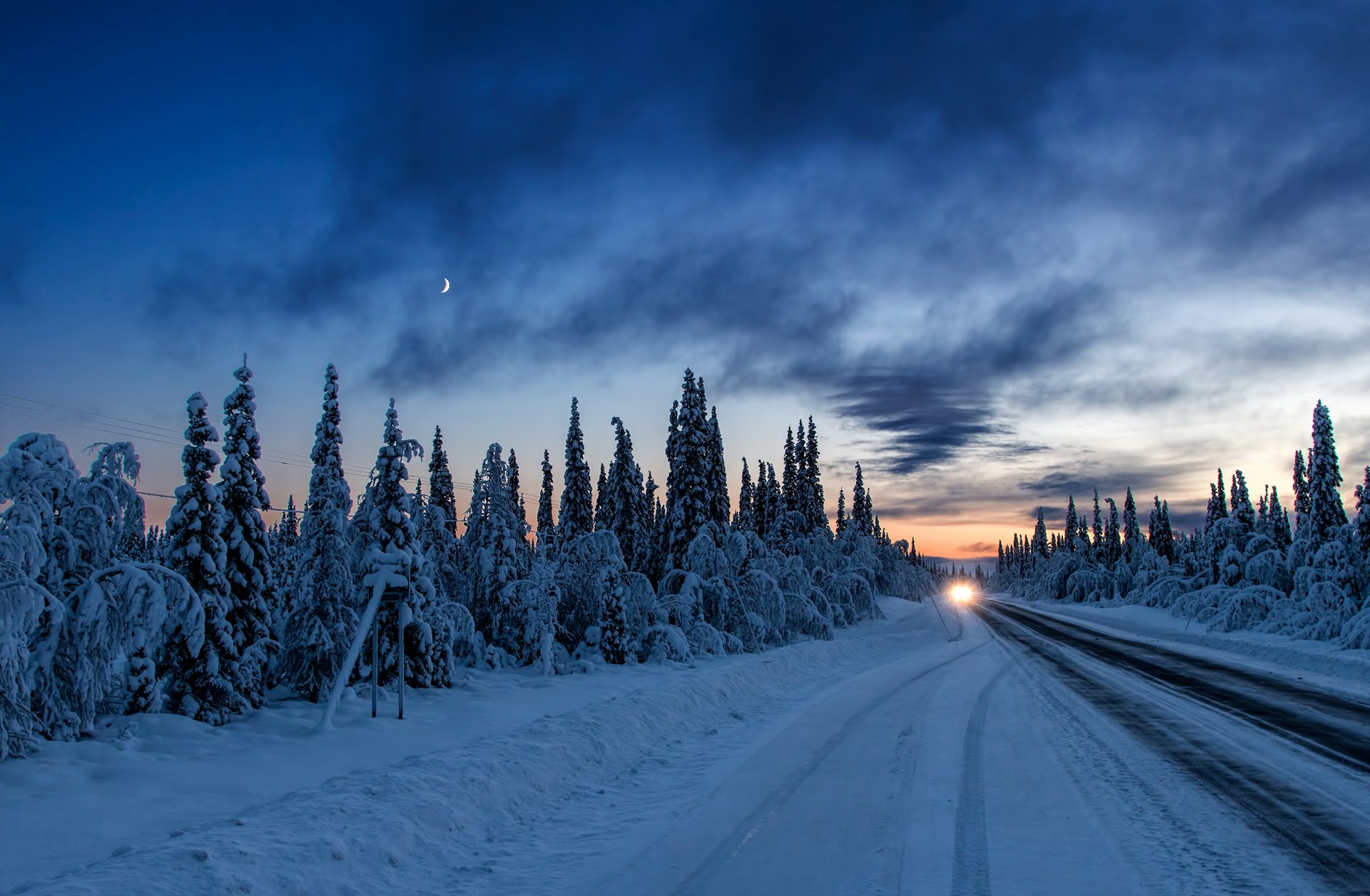 A snow covered road in arctic Sweden in late evening lined by trees covered in snow