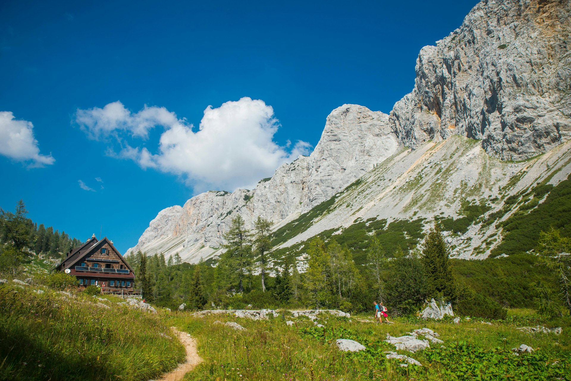 Two hikers follow a path leading to a wood cabin in a rocky landscape