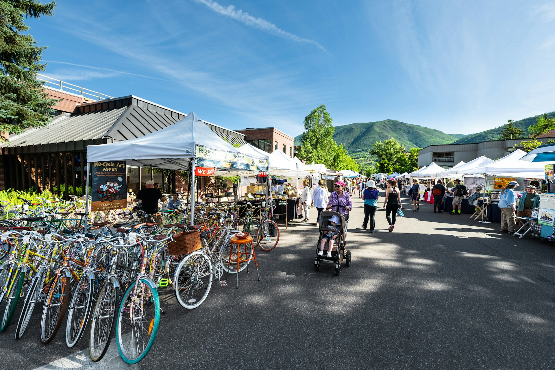 Vendors selling vintage bicycles at stall stand in farmers market with people walking in outdoor summer street