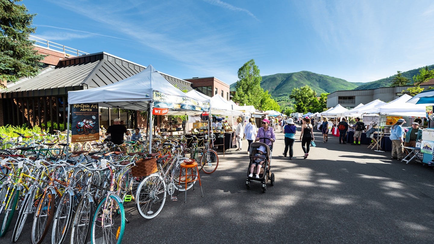 Aspen, USA - July 6, 2019: Vendors selling vintage bicycles at stall stand in farmers market with people walking in outdoor summer street
