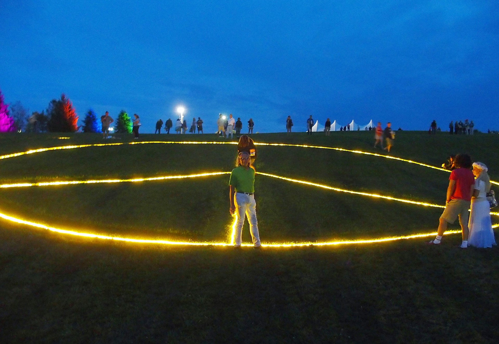 A man stands in front of a large peace sign light stretches across the ground in Bethel Woods.  