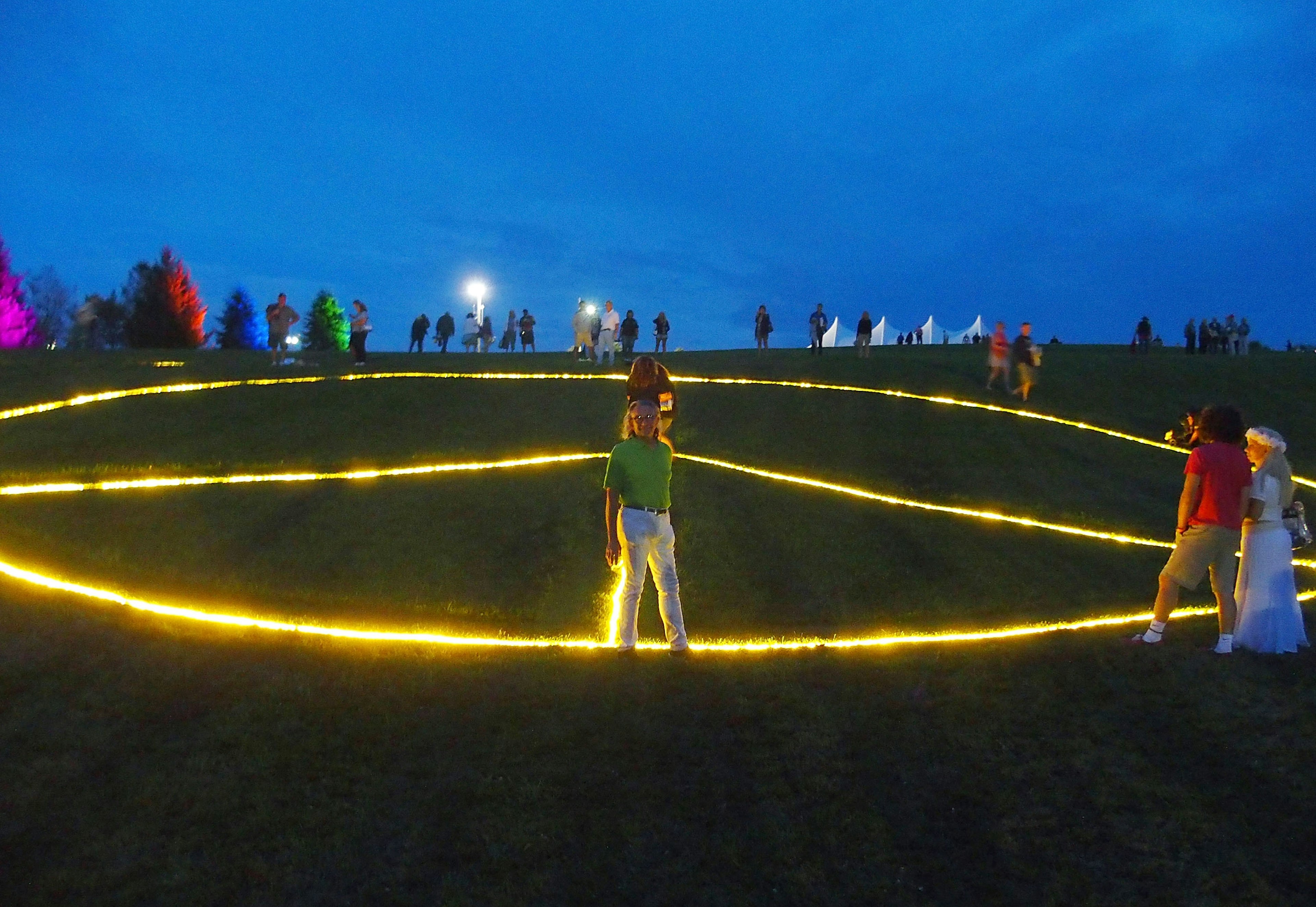 A man stands in front of a large peace sign light stretches across the ground in Bethel Woods.