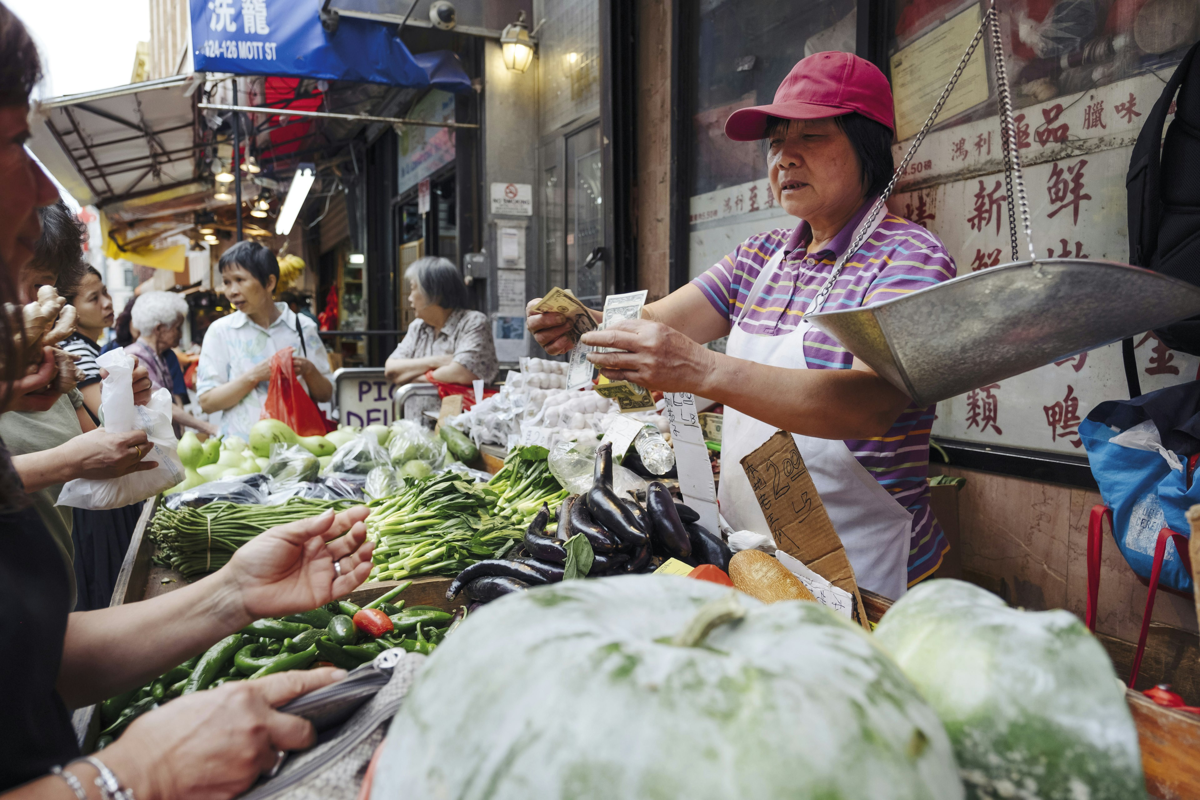 A street vendor selling produce in Chinatown, New York, and counting money.