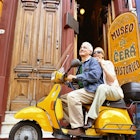 An older couple rides a yellow scooter along a street in Buenos Aires