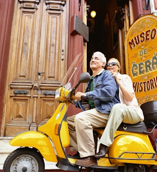 An older couple rides a yellow scooter along a street in Buenos Aires