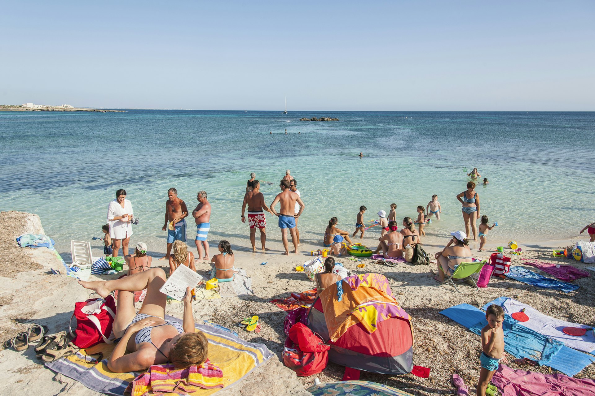 Families sunbathe on the rocks and paddle in the clear blue sea at Cala Rossa