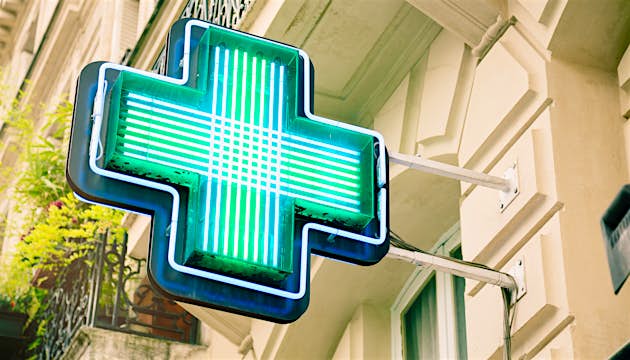 French pharmacy neon sign in front of Parisian apartments.