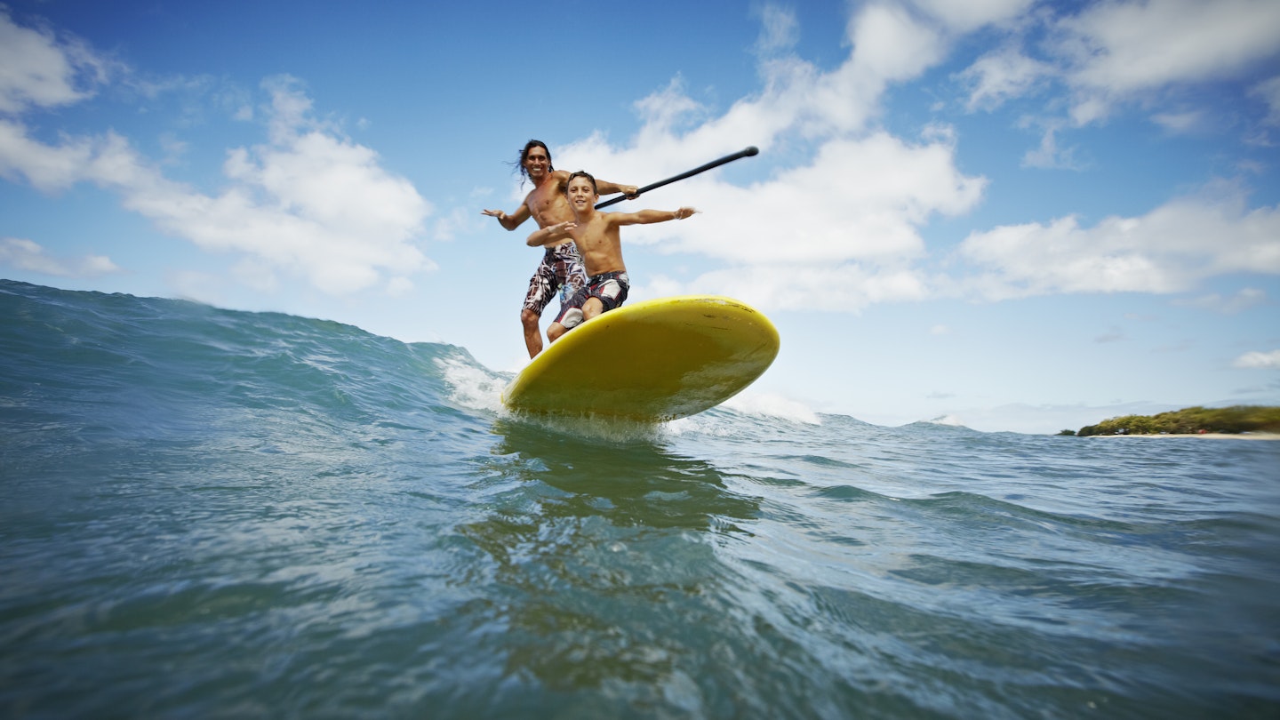 A father and son riding a wave on a paddleboard on Maui