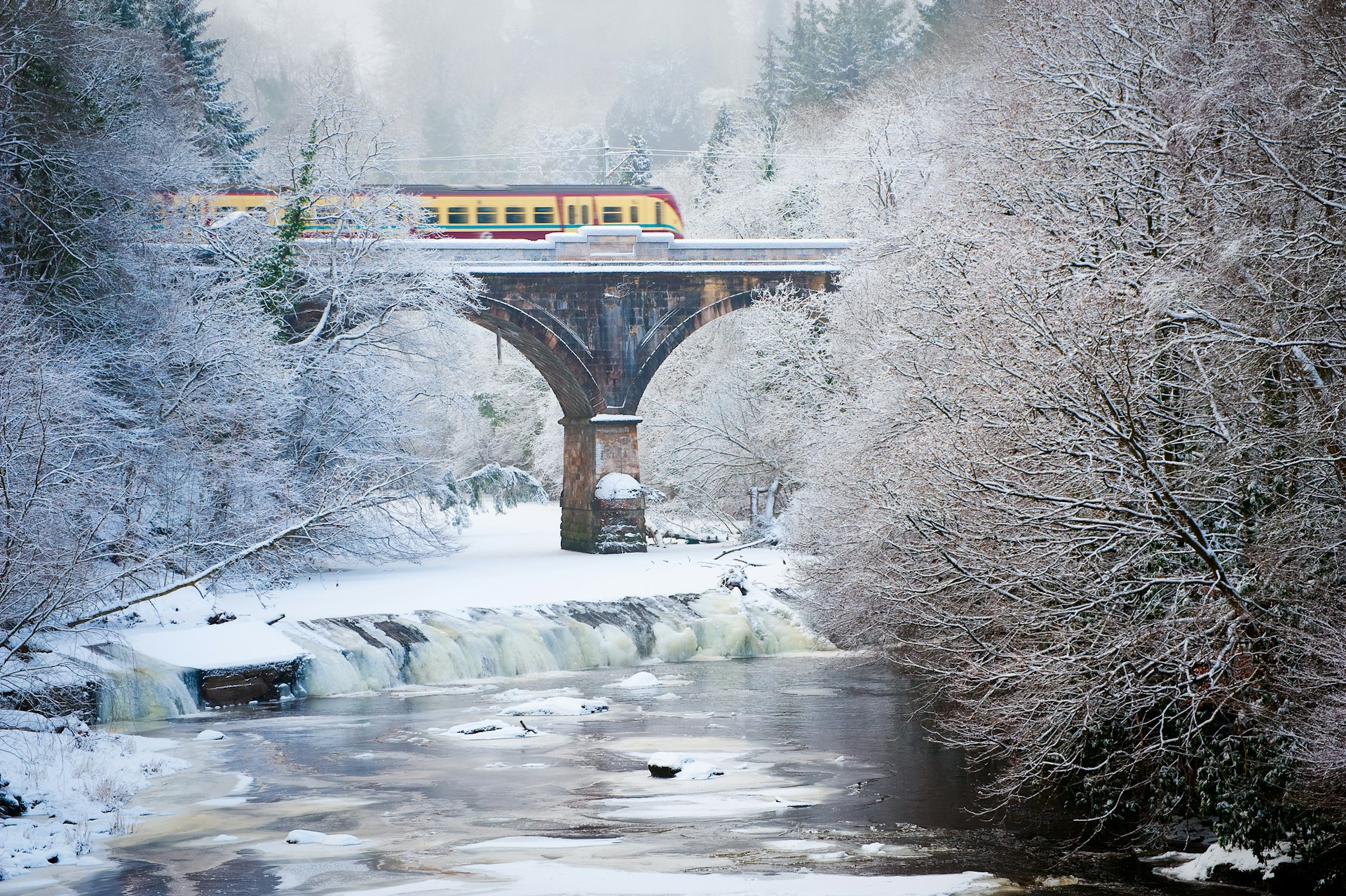 Train crossing a stone bridge over water on a frosty, snowy day