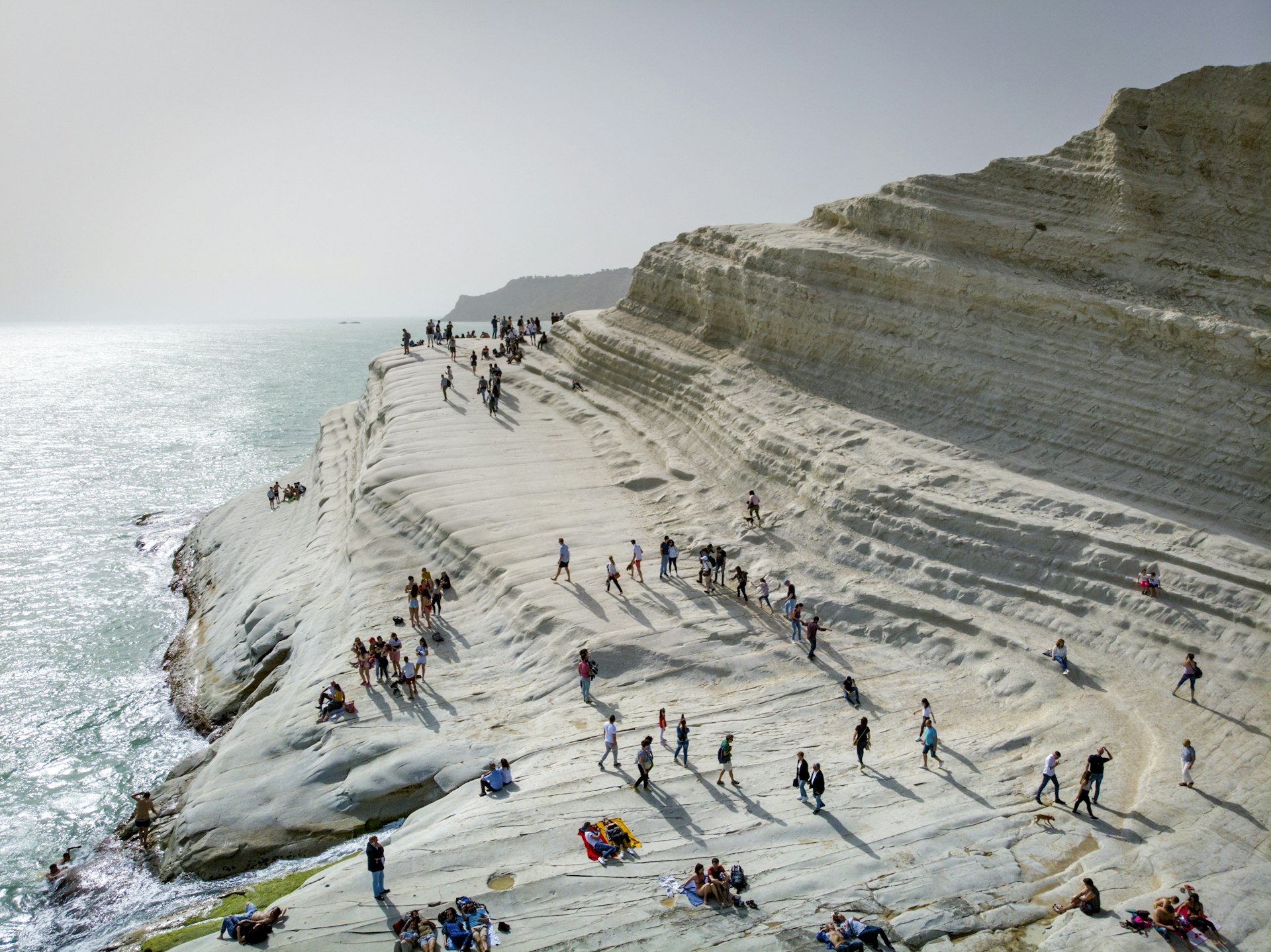 People climbing on a smooth wave of white rocks at the edge of the sea 