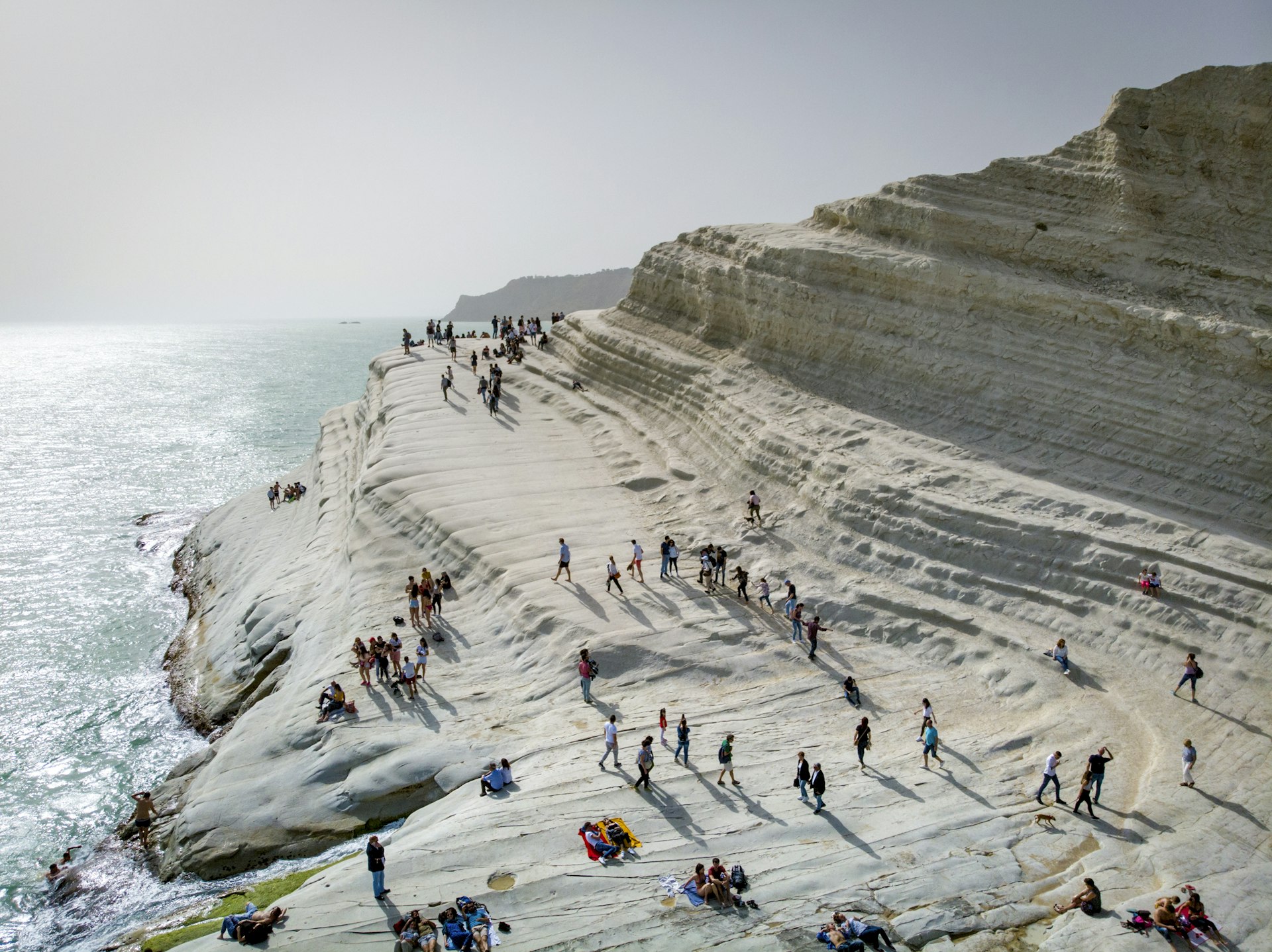 People climbing on a smooth wave of white rocks at the edge of the sea