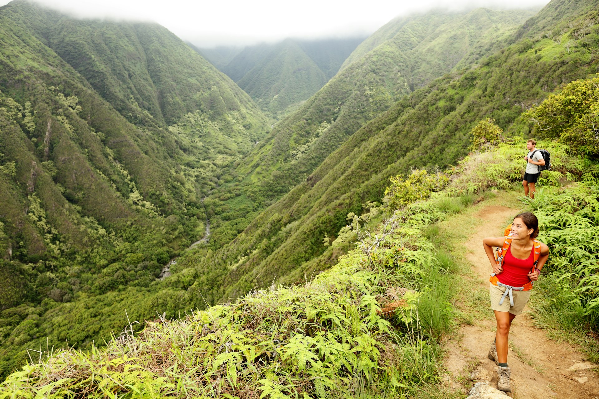 A young couple hiking a forest ridge smile as they hike Hawaii's Waihee Ridge Trail on Maui with the green mountains in the background