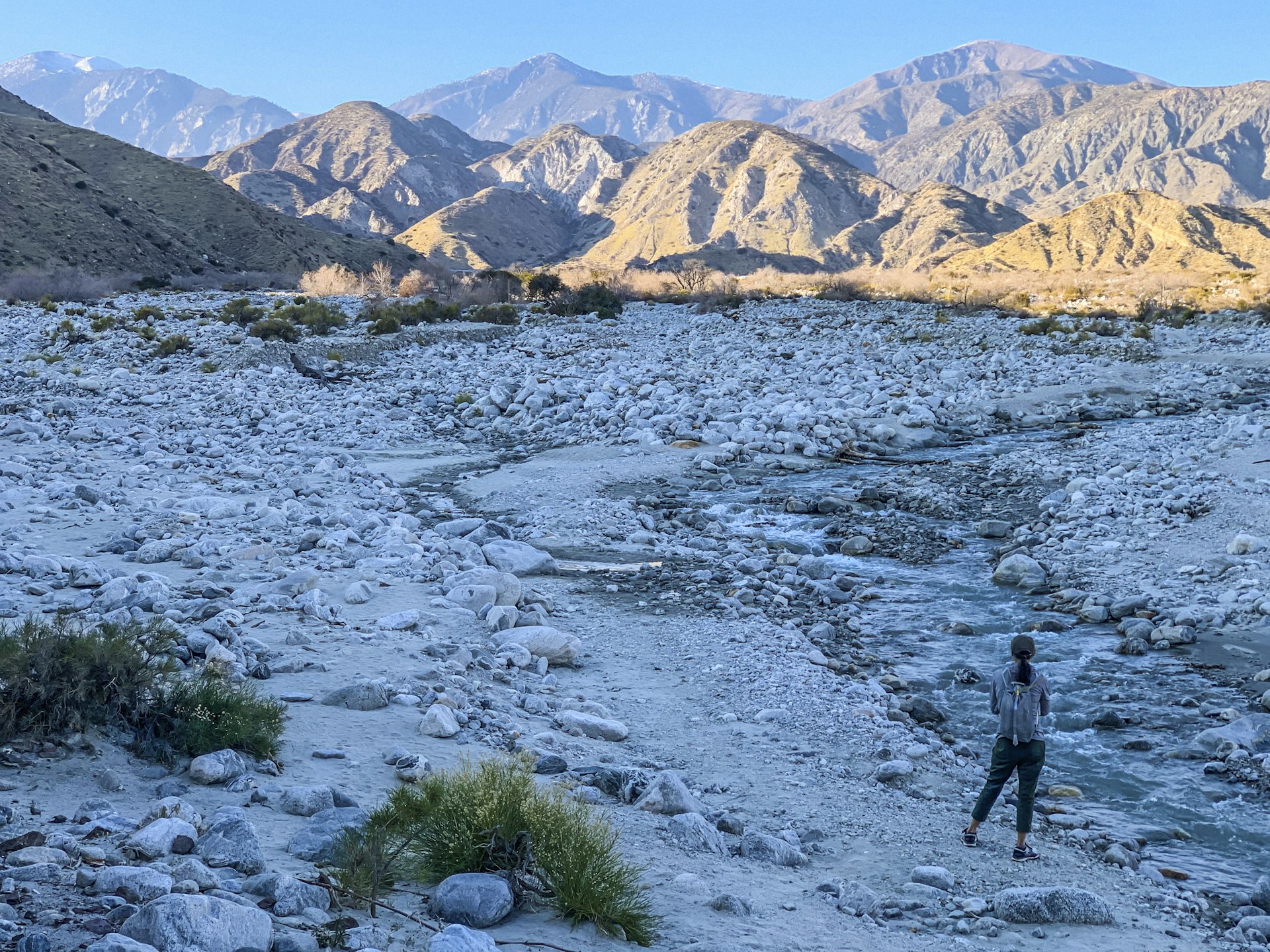 Woman hiker in a rocky landscape near a fast-flowing stream looking towards a mountain range