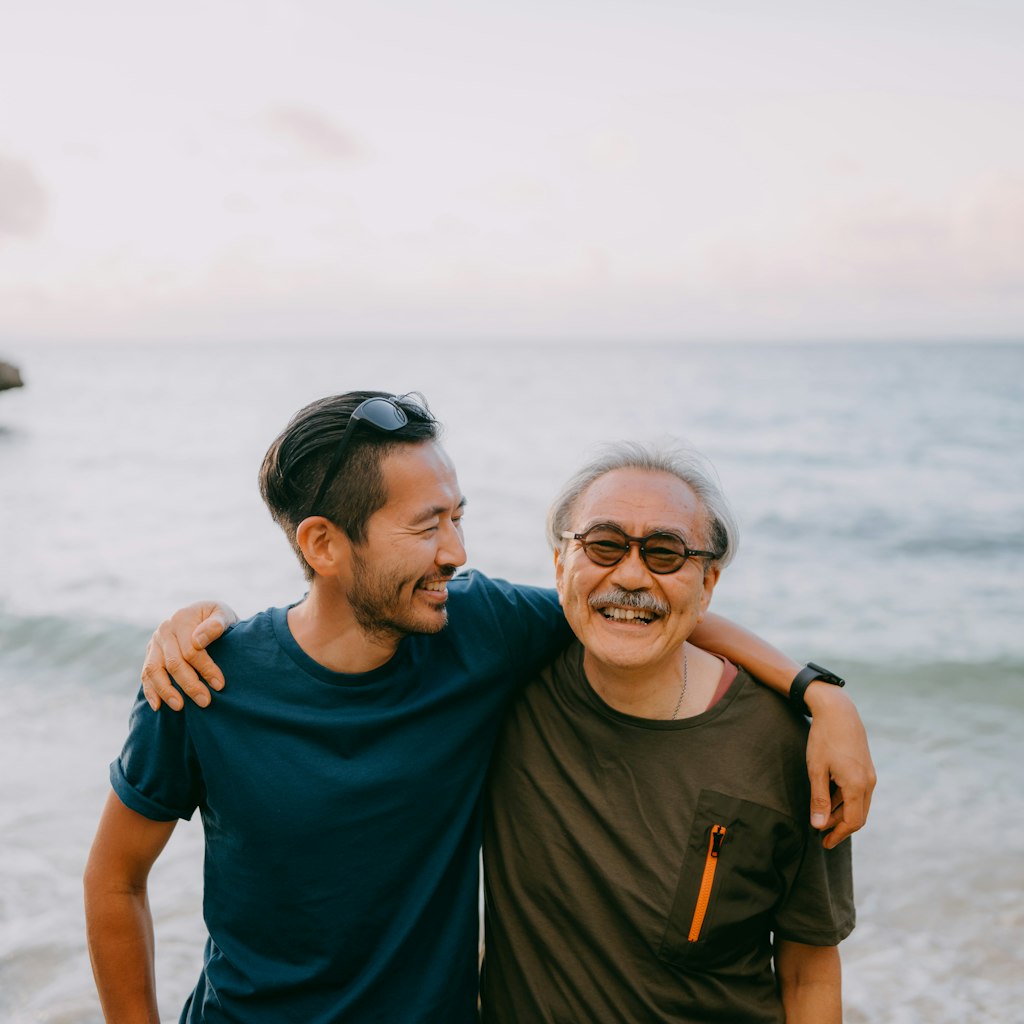 Japanese senior father and adult son having a good time on beach at sunset, Ishigaki Island, Okinawa, Japan