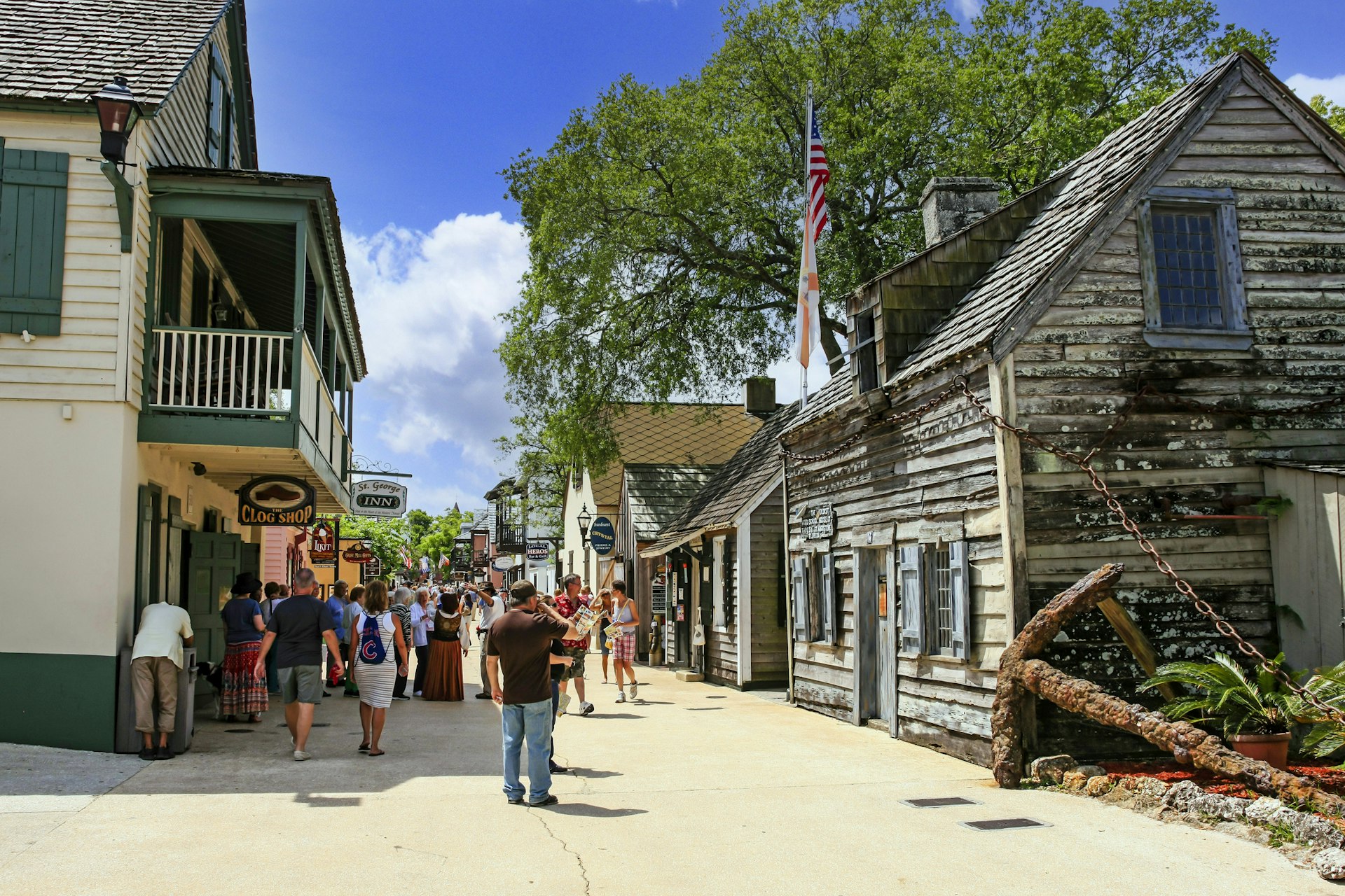 A pedestrian street scene with tourists mingling around in front of an old wooden school building