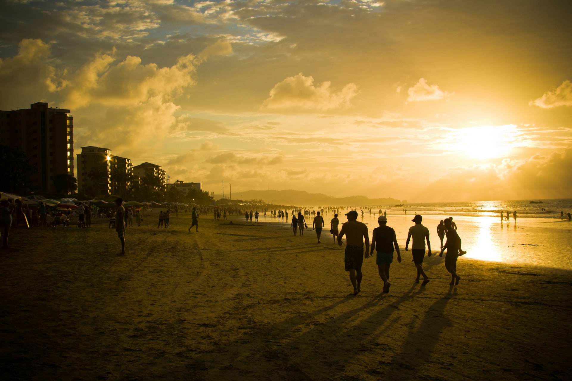 Groups of people in silhouette walking on a beach as the sun sets in the sky