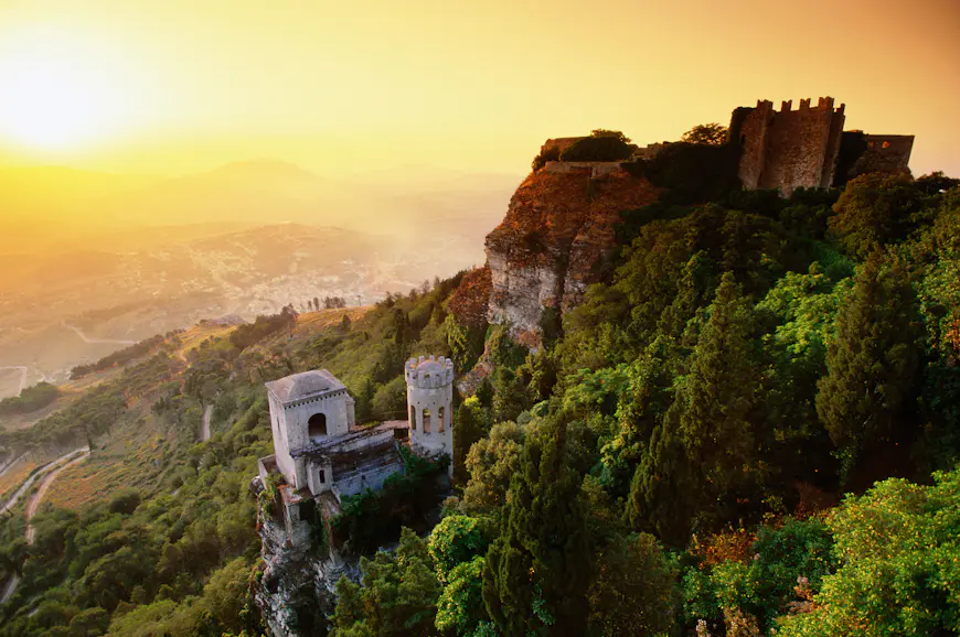 Que ver en Sicilia Un castillo medieval en lo alto de un acantilado al atardecer con vistas que se extienden sobre las colinas de abajo