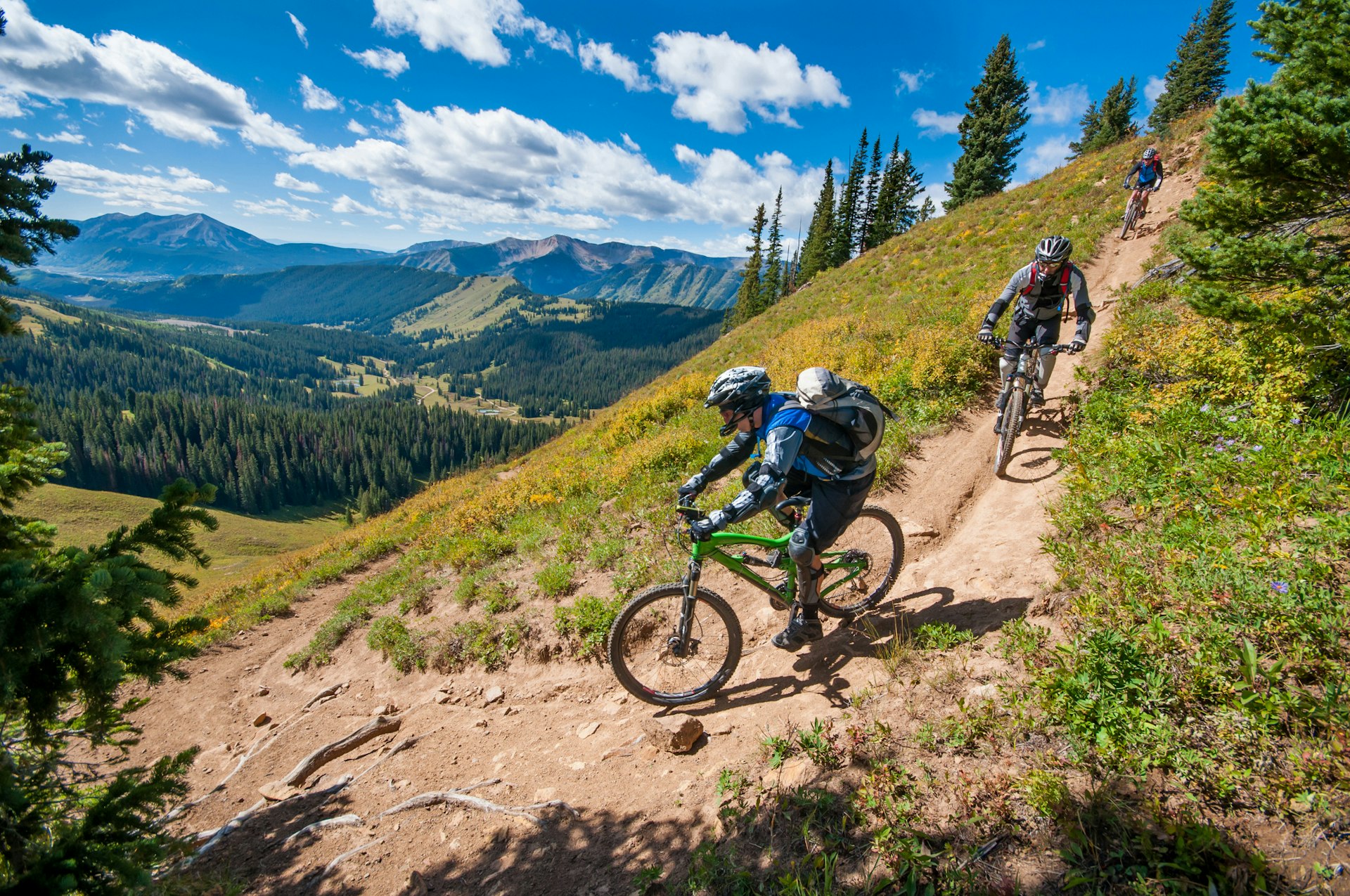 Three mountain bikers descend a steep path amid beautiful views