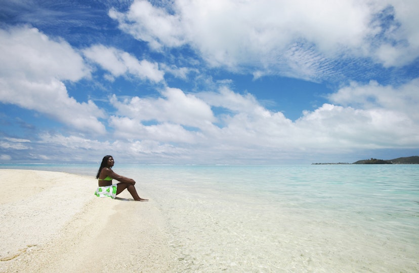 A women sitting on a white sand beach at Bora Bora, French Polynesia