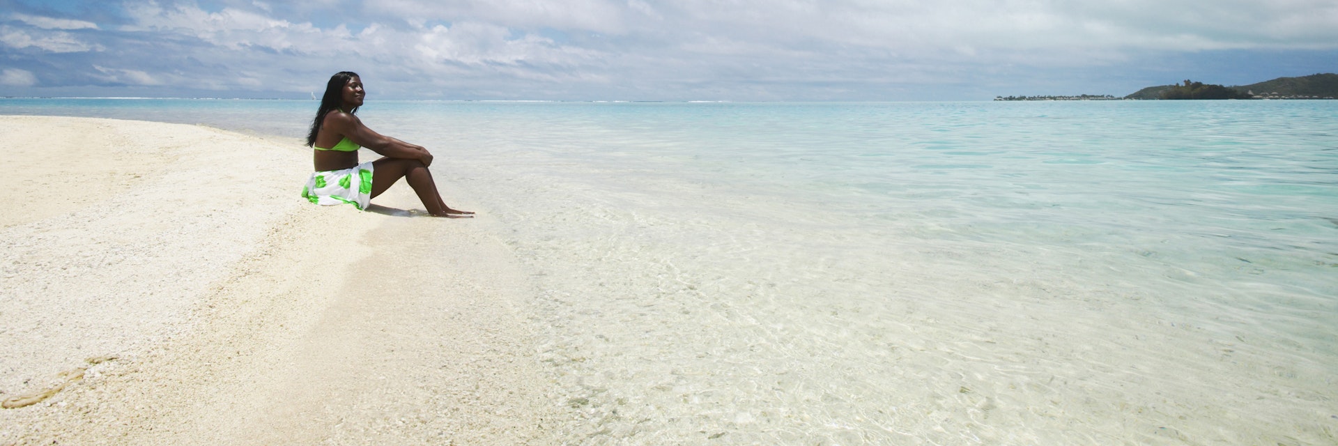 A women sitting on a white sand beach at Bora Bora, French Polynesia