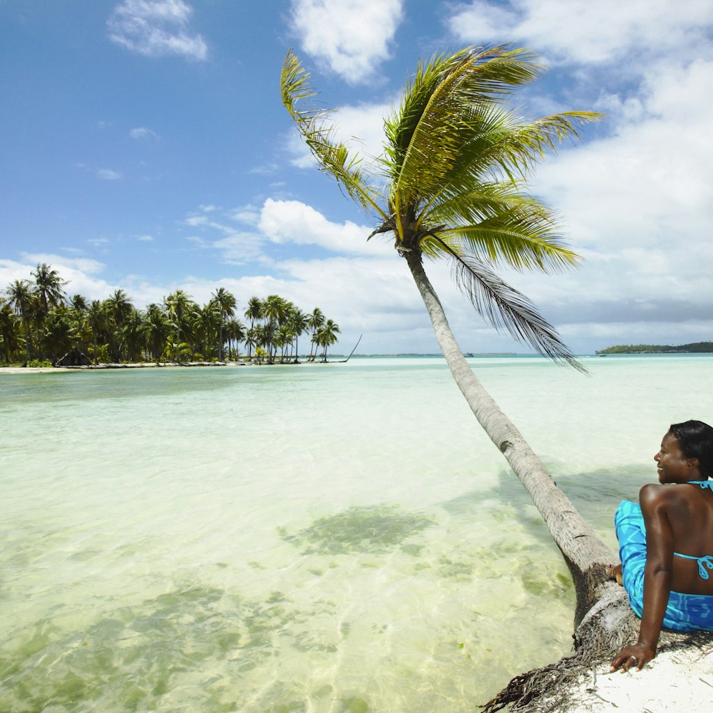 A woman sitting by a palm tree on a beach in Bora Bora