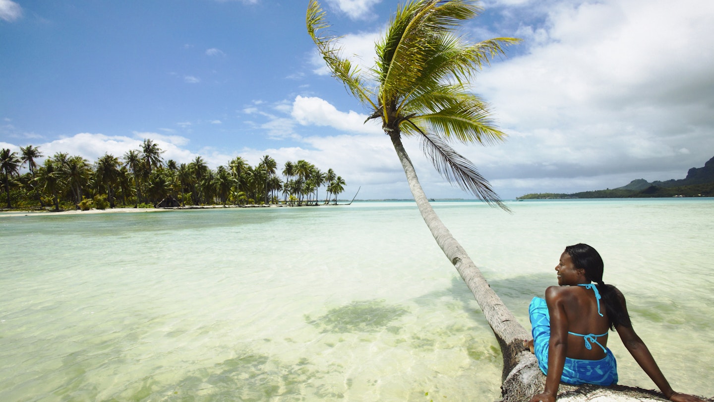 A woman sitting by a palm tree on a beach in Bora Bora