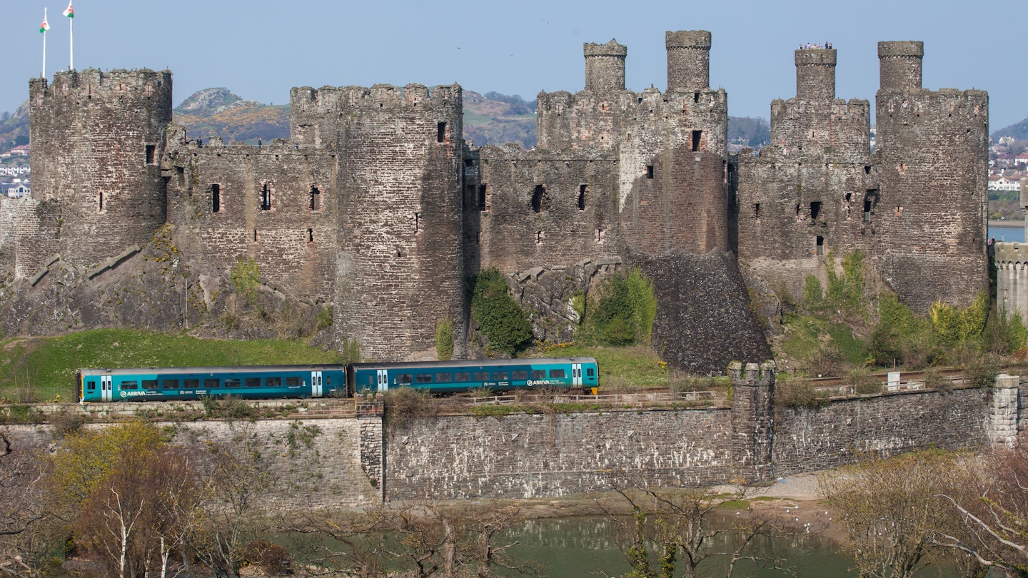 Comwy, Wales - April 9, 2015: Conwy Castle and a Passenger Train North Wales. The railway lone runs along the base of the medeval castle and the Virgin Trains service passes the castle. People can be seen on the catsle walls. The sky is clear and blue.