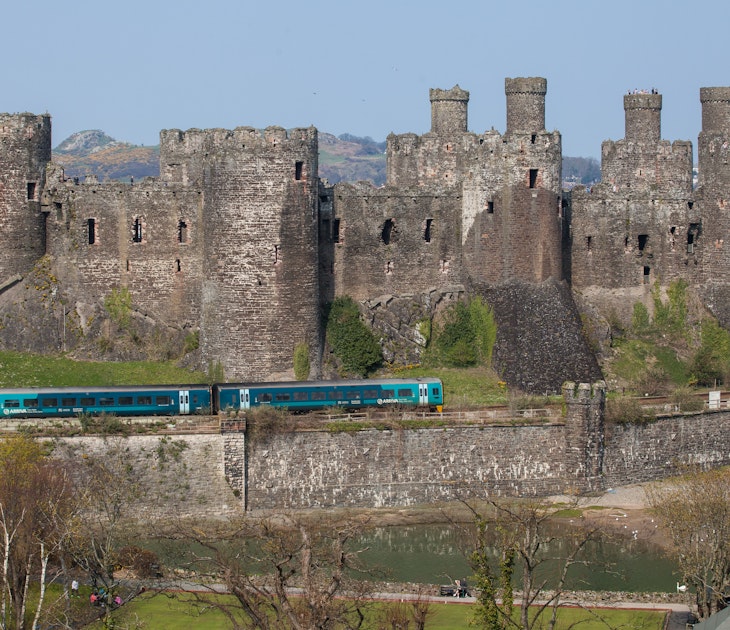 Comwy, Wales - April 9, 2015: Conwy Castle and a Passenger Train North Wales. The railway lone runs along the base of the medeval castle and the Virgin Trains service passes the castle. People can be seen on the catsle walls. The sky is clear and blue.