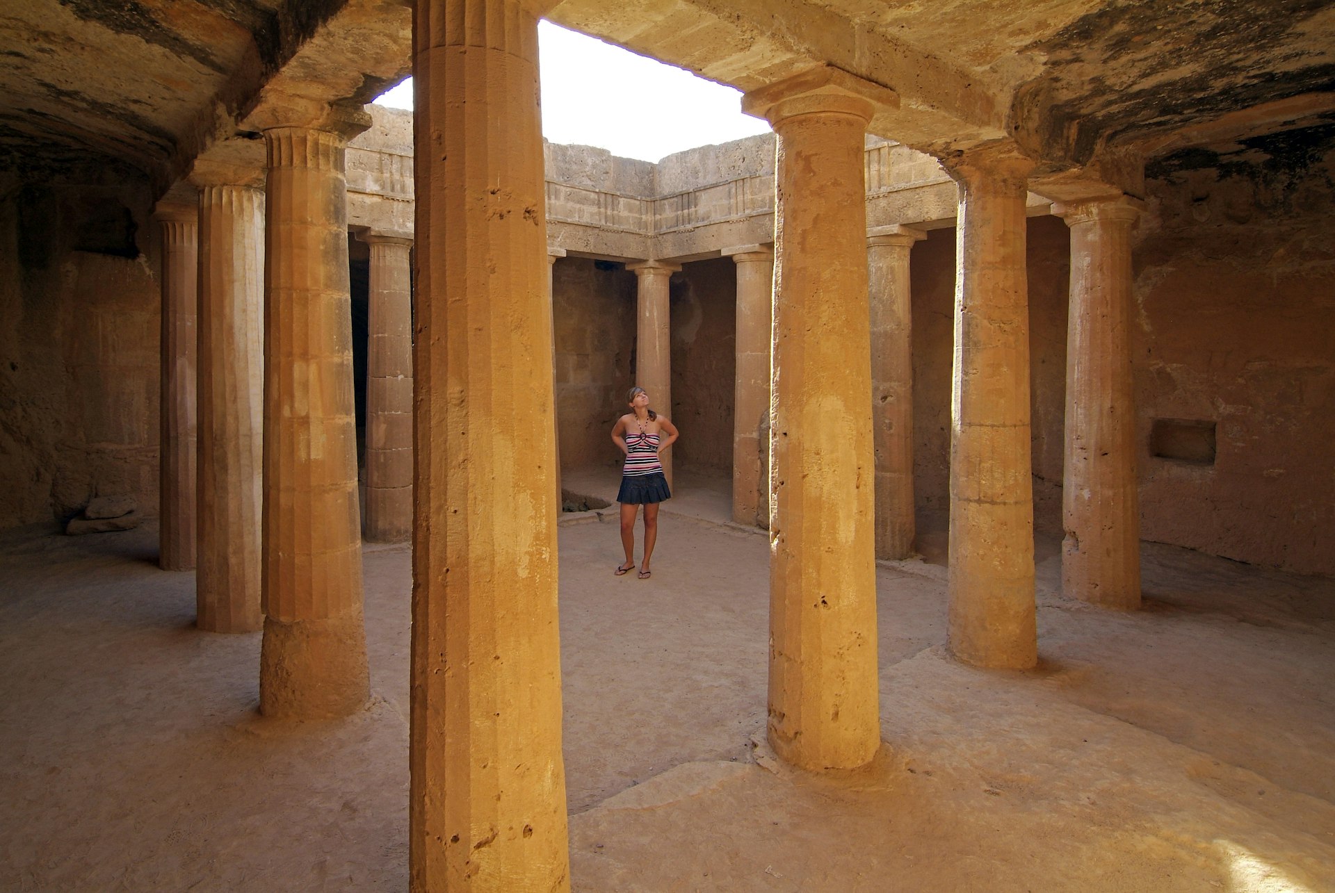 Woman walking past columns of tomb in the Tomb of the Kings, Pafos