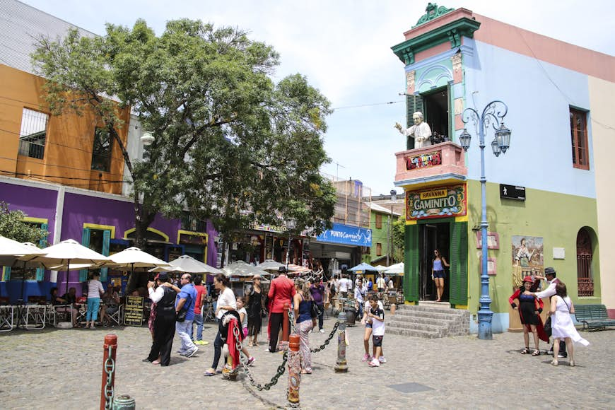 Tango dancers pose for photos with tourists in front of a brightly painted building in El Caminito, Buenos Aires