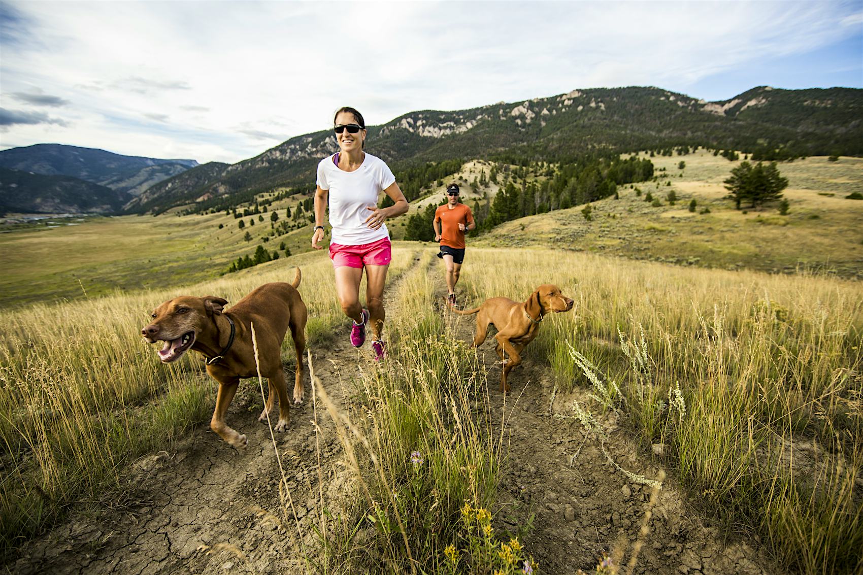 Couple trail running with two dogs on Montana hillside near Bozeman