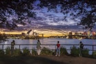 Four people photographing the Sydney Opera House and Sydney Harbour Bridge from Mrs Macquaries Chair at dusk.