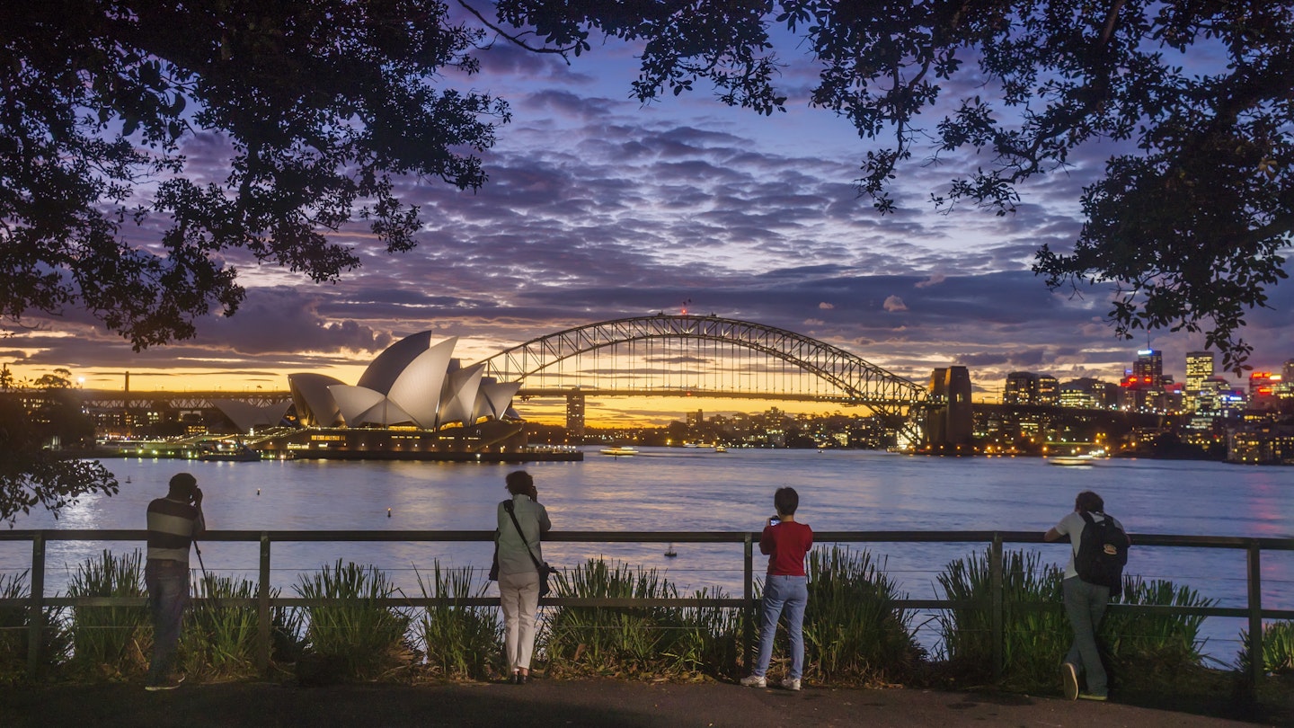 Four people photographing the Sydney Opera House and Sydney Harbour Bridge from Mrs Macquaries Chair at dusk.